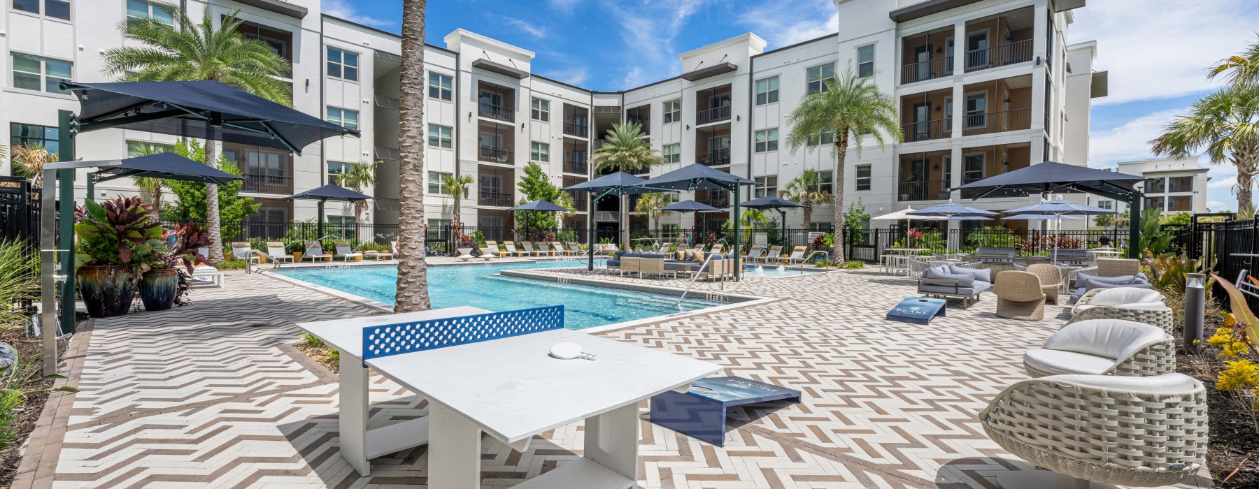 Three-Bedroom Luxury Apartments In Naples, FL - The Pearl Founders Square Apartments - Resort-Style Pool With with Sun Shelf, Cabanas, Plenty Of Seating Areas, Cornhole, And Ping Pong Table